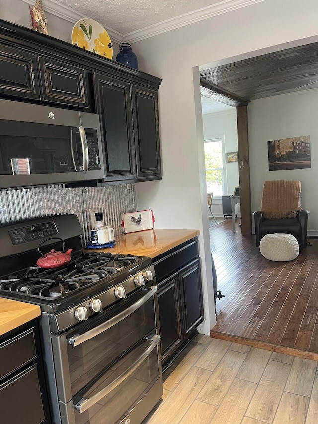 kitchen featuring light wood-type flooring, wooden counters, ornamental molding, stainless steel appliances, and a textured ceiling