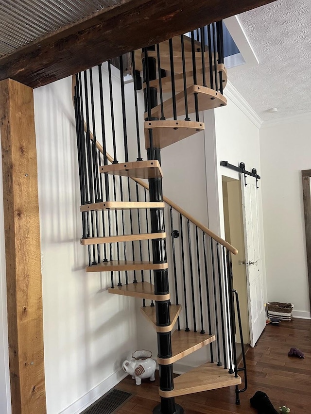 staircase featuring wood-type flooring, a barn door, crown molding, and a textured ceiling