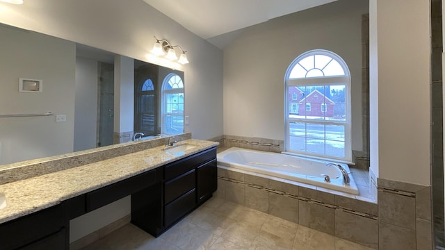 bathroom with vanity, vaulted ceiling, a healthy amount of sunlight, and a relaxing tiled tub