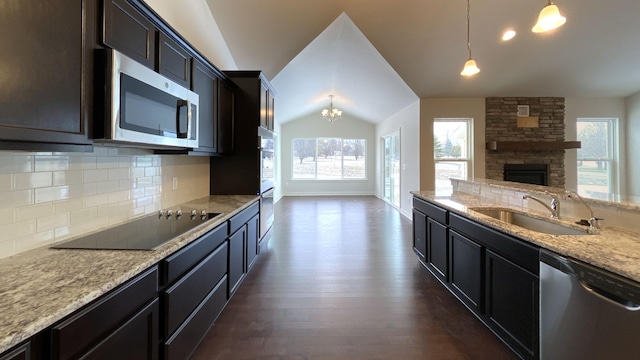 kitchen featuring lofted ceiling, sink, hanging light fixtures, stainless steel appliances, and light stone counters