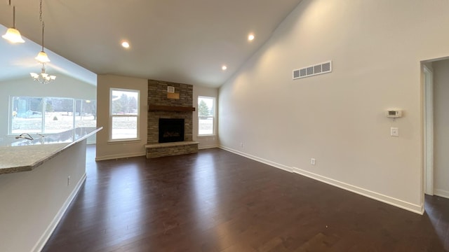 unfurnished living room with a stone fireplace, a chandelier, high vaulted ceiling, and dark hardwood / wood-style flooring