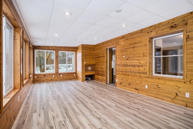 unfurnished living room featuring a paneled ceiling, light hardwood / wood-style floors, and wood walls