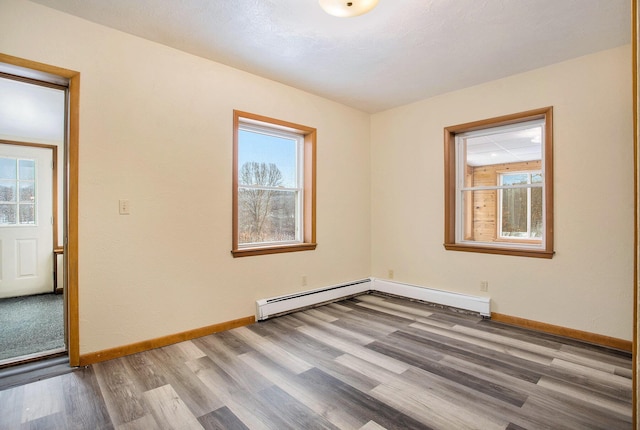 empty room with a baseboard heating unit, wood-type flooring, and a healthy amount of sunlight