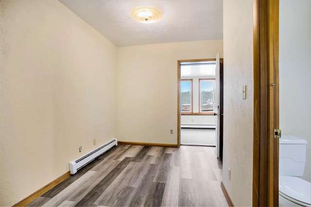 empty room featuring hardwood / wood-style floors, a textured ceiling, and baseboard heating