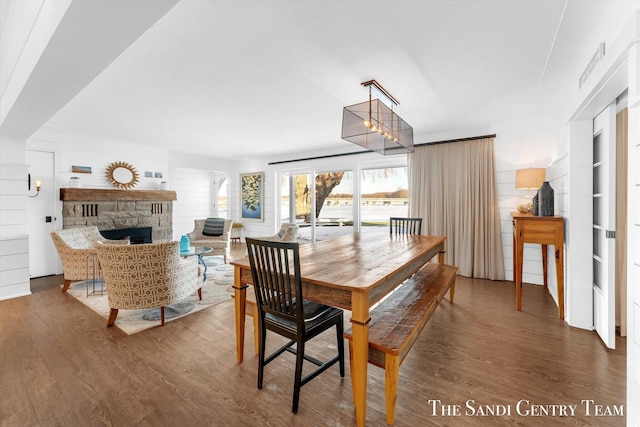 dining room featuring a stone fireplace, an inviting chandelier, and wood finished floors