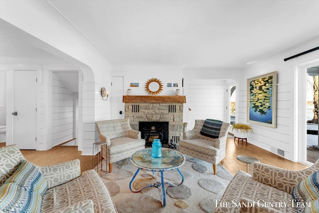 living area featuring arched walkways, a fireplace, wood finished floors, and visible vents