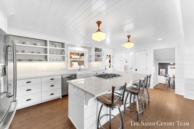 kitchen featuring dark wood-type flooring, a center island, stainless steel appliances, open shelves, and a sink