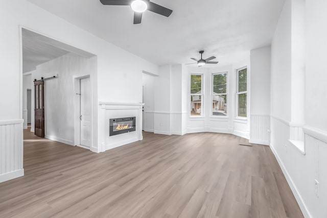 unfurnished living room with ceiling fan, a barn door, heating unit, and light wood-type flooring