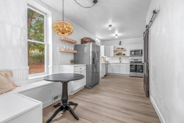 kitchen featuring sink, pendant lighting, stainless steel appliances, a barn door, and white cabinets