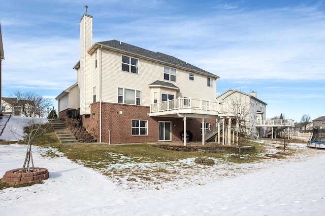 snow covered rear of property with an outdoor fire pit, a deck, and a trampoline