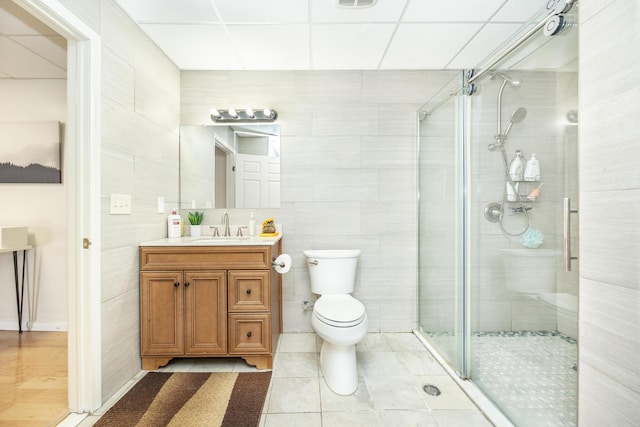 bathroom with vanity, toilet, a shower with door, and tile walls