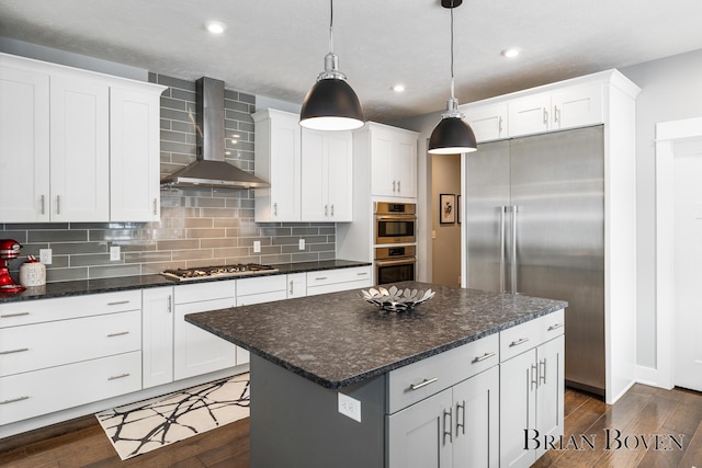 kitchen featuring wall chimney range hood, hanging light fixtures, stainless steel appliances, white cabinets, and a kitchen island