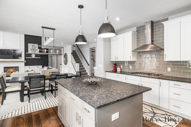 kitchen with white cabinetry, hanging light fixtures, a center island, stainless steel gas cooktop, and wall chimney range hood