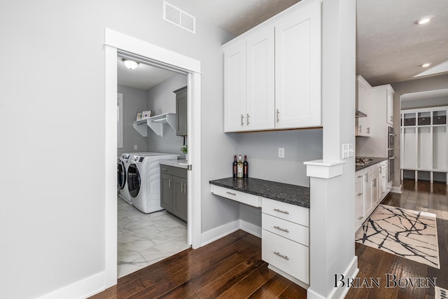 kitchen featuring dark wood-type flooring, white cabinetry, built in desk, washer and dryer, and dark stone counters