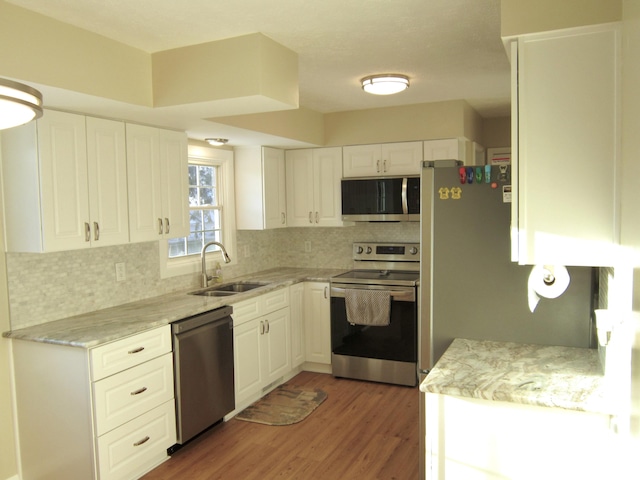 kitchen with white cabinets, a sink, stainless steel appliances, light wood-style floors, and backsplash