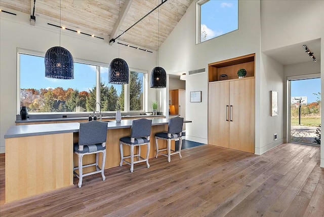 kitchen featuring a kitchen bar, decorative light fixtures, high vaulted ceiling, wooden ceiling, and light wood-type flooring