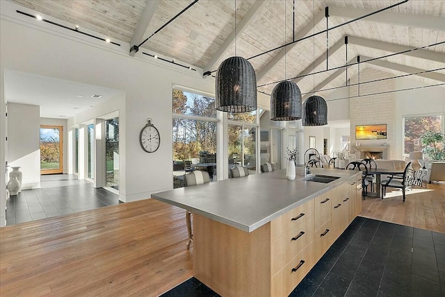 kitchen with a fireplace, light brown cabinetry, an island with sink, sink, and hardwood / wood-style flooring