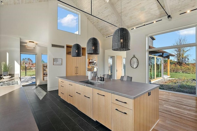 kitchen with light brown cabinetry, an island with sink, hanging light fixtures, and wooden ceiling