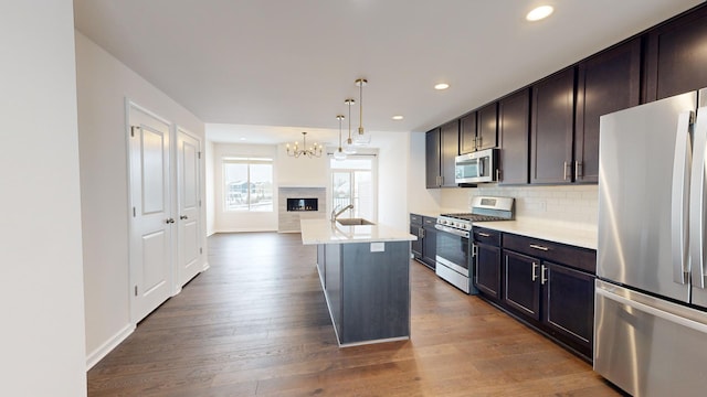 kitchen featuring pendant lighting, appliances with stainless steel finishes, a kitchen island with sink, dark hardwood / wood-style floors, and decorative backsplash