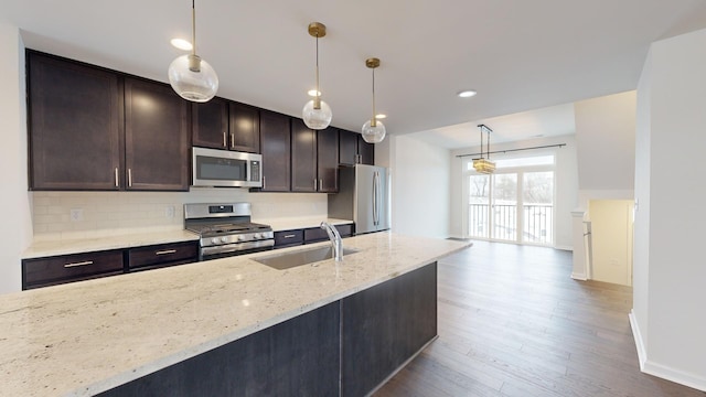 kitchen featuring appliances with stainless steel finishes, pendant lighting, sink, light stone counters, and dark brown cabinets