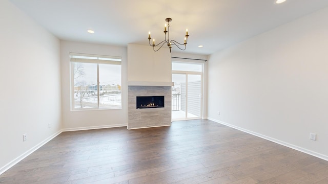 unfurnished living room with a tiled fireplace, hardwood / wood-style floors, a notable chandelier, and plenty of natural light