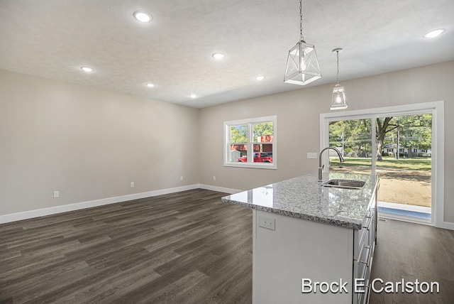 kitchen featuring a kitchen island with sink, sink, decorative light fixtures, and dark hardwood / wood-style flooring