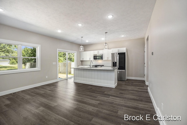 kitchen featuring white cabinetry, hanging light fixtures, stainless steel appliances, a kitchen island with sink, and backsplash