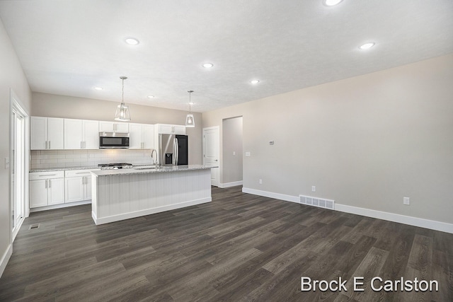 kitchen with appliances with stainless steel finishes, pendant lighting, white cabinetry, an island with sink, and dark hardwood / wood-style flooring