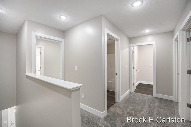 hallway featuring a textured ceiling and dark colored carpet