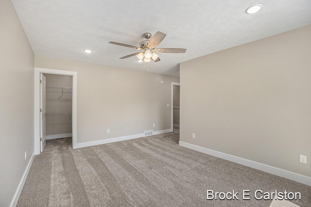 unfurnished bedroom with a walk in closet, carpet floors, a textured ceiling, and ceiling fan