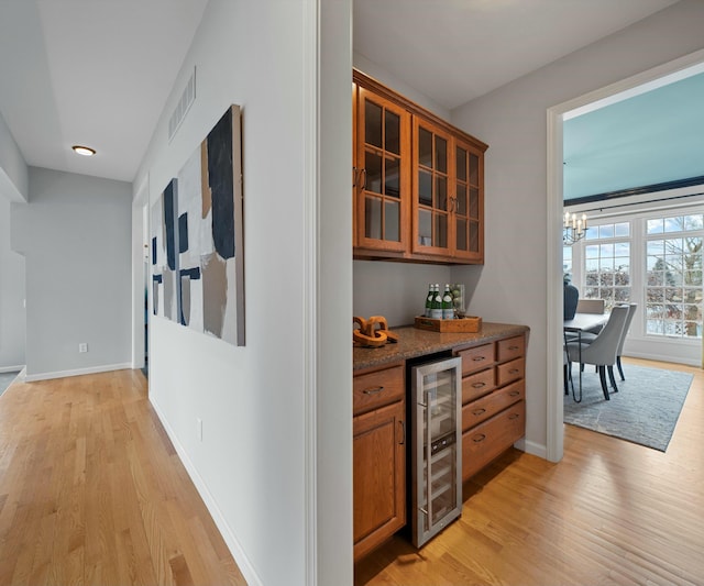 bar featuring a chandelier, dark stone countertops, beverage cooler, and light hardwood / wood-style floors