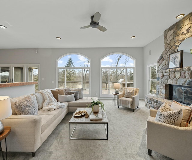 carpeted living room featuring ceiling fan and a stone fireplace