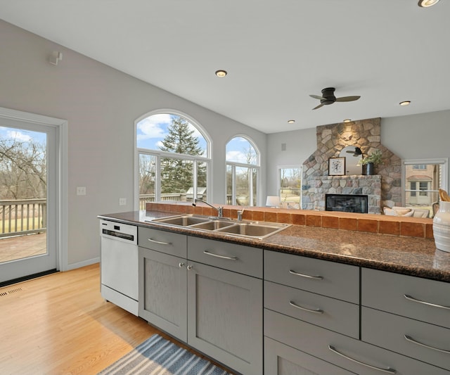 kitchen with a stone fireplace, sink, gray cabinetry, white dishwasher, and light wood-type flooring