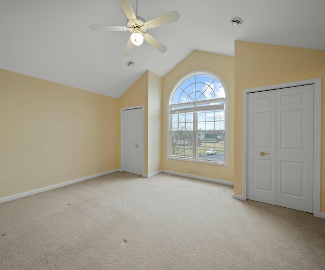 unfurnished bedroom featuring ceiling fan, vaulted ceiling, light carpet, and two closets