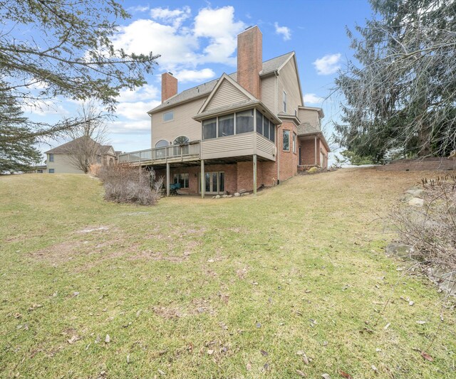 back of house featuring a wooden deck, a sunroom, and a lawn