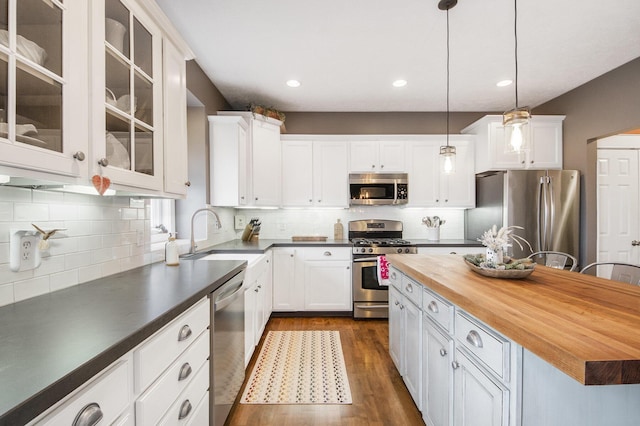 kitchen with butcher block countertops, decorative light fixtures, sink, white cabinets, and stainless steel appliances