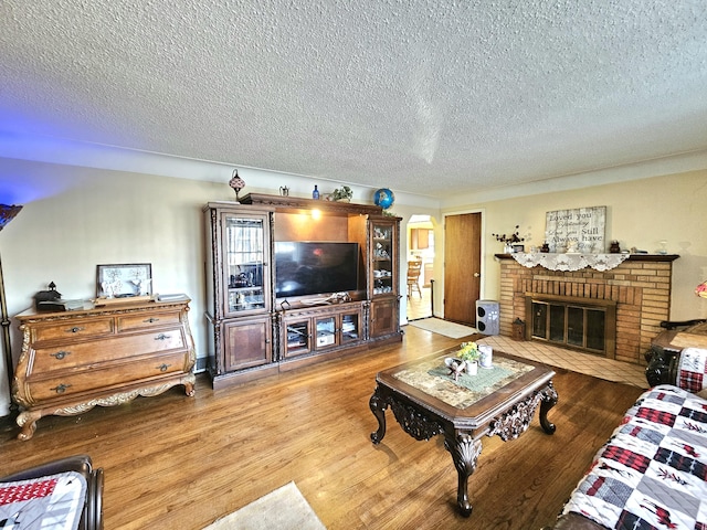 living room with wood-type flooring, a brick fireplace, and a textured ceiling