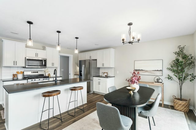 kitchen with white cabinetry, appliances with stainless steel finishes, hanging light fixtures, and a center island with sink