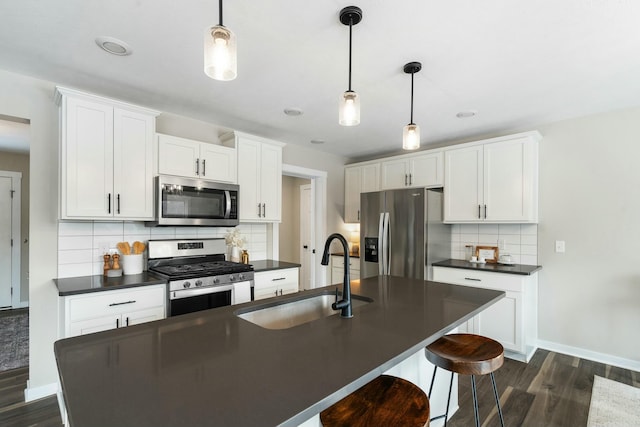 kitchen featuring an island with sink, appliances with stainless steel finishes, decorative light fixtures, and sink