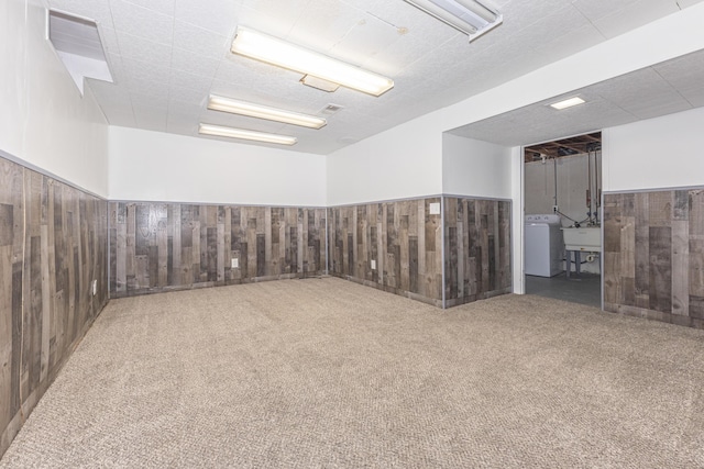 carpeted spare room featuring washer / dryer, sink, and wood walls