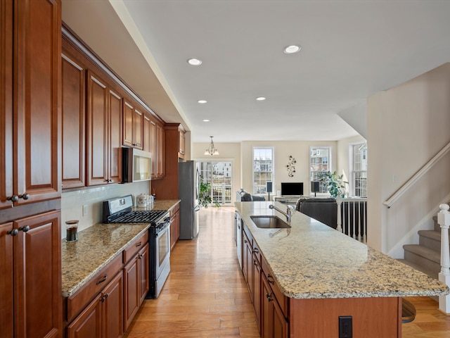 kitchen with appliances with stainless steel finishes, sink, a kitchen island with sink, light stone counters, and light hardwood / wood-style flooring