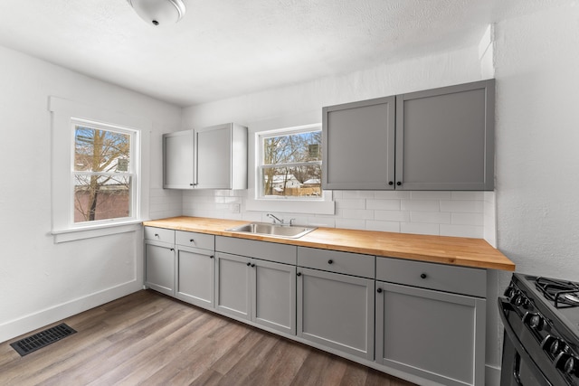 kitchen with sink, black range with gas cooktop, gray cabinetry, tasteful backsplash, and wood counters