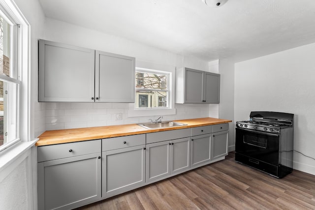 kitchen featuring black gas range oven, sink, wooden counters, gray cabinetry, and backsplash