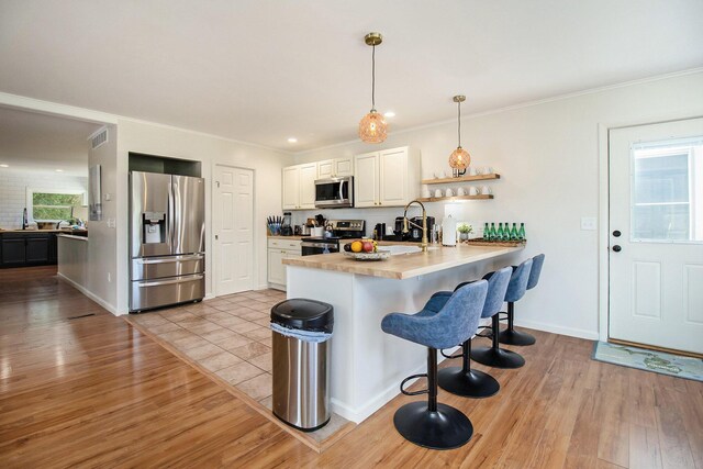 kitchen featuring stainless steel appliances, hanging light fixtures, light hardwood / wood-style flooring, and kitchen peninsula