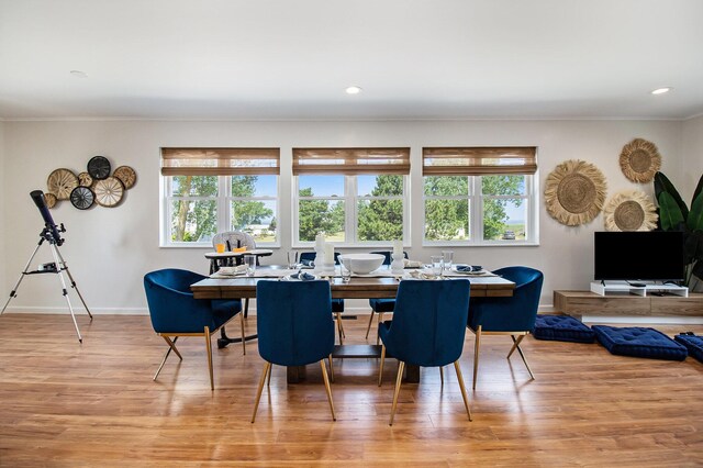 dining space with ornamental molding and light hardwood / wood-style flooring