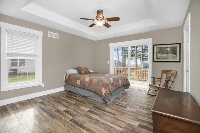 bedroom with dark wood-type flooring, ceiling fan, access to exterior, and a raised ceiling