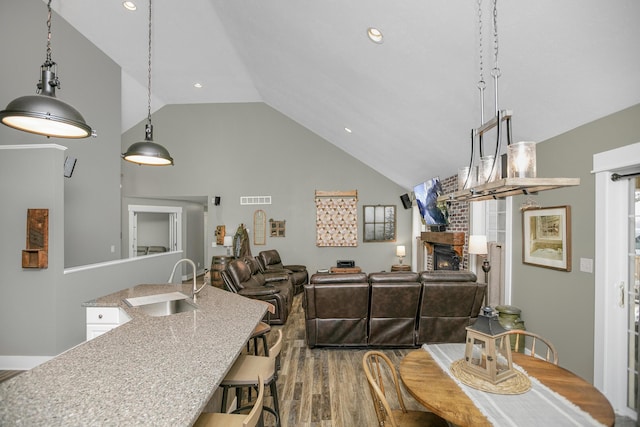 dining area with hardwood / wood-style flooring, high vaulted ceiling, a fireplace, and sink