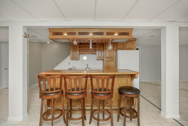 bar with a drop ceiling, light tile patterned floors, and white refrigerator