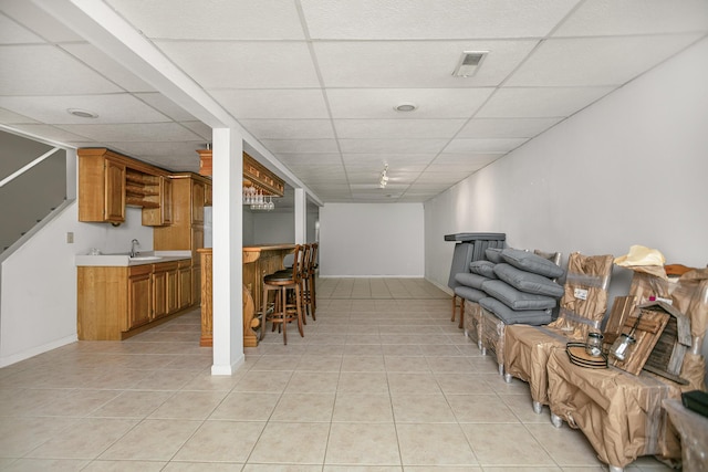 basement featuring light tile patterned flooring, wet bar, and a drop ceiling