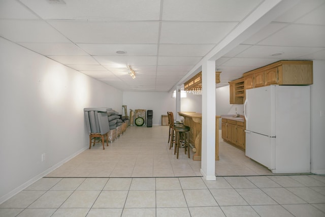 basement featuring white refrigerator, a paneled ceiling, indoor wet bar, and light tile patterned floors